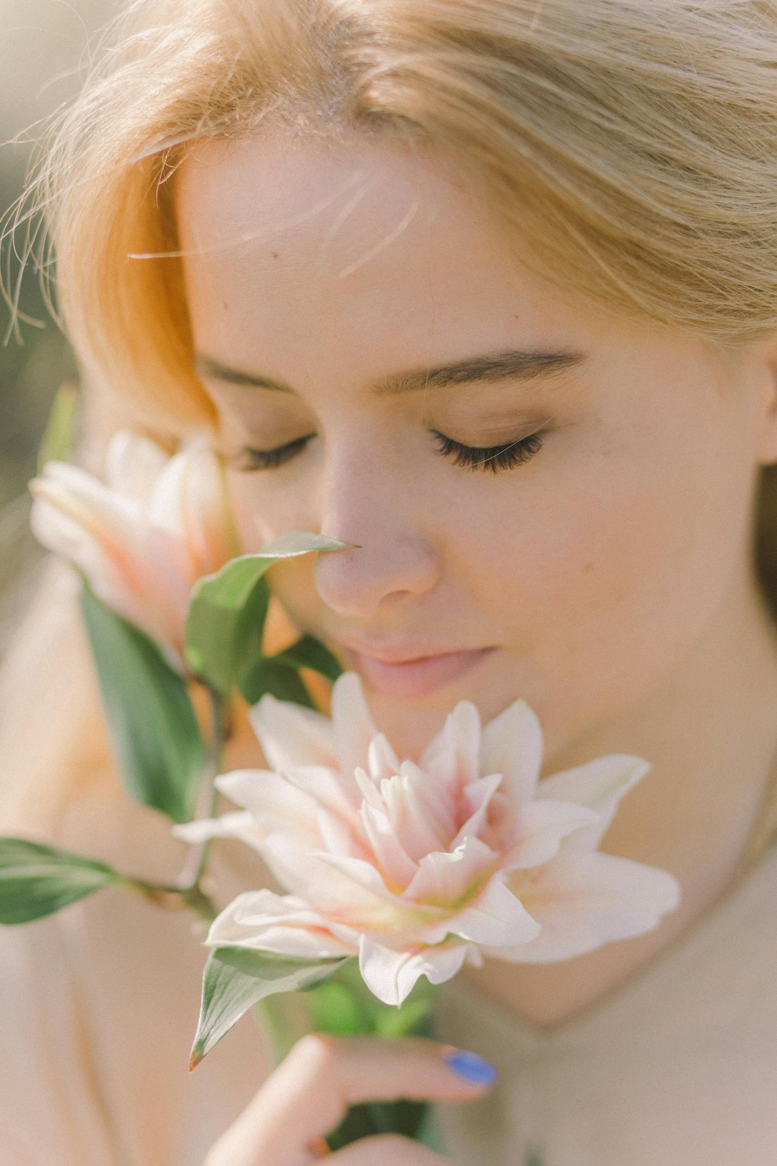 Close-up of a woman with closed eyes smelling blooming lilies outdoors on a sunny day.