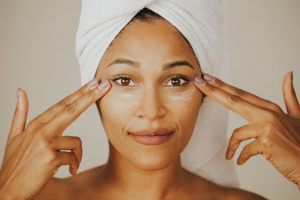 Woman applying facial treatment with a towel wrapped on her head, highlighting skincare routine.